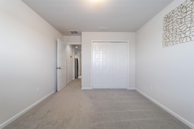 unfurnished bedroom with light colored carpet, a closet, and a textured ceiling