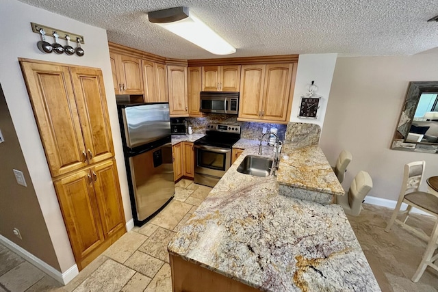 kitchen with appliances with stainless steel finishes, a peninsula, light stone countertops, a sink, and backsplash