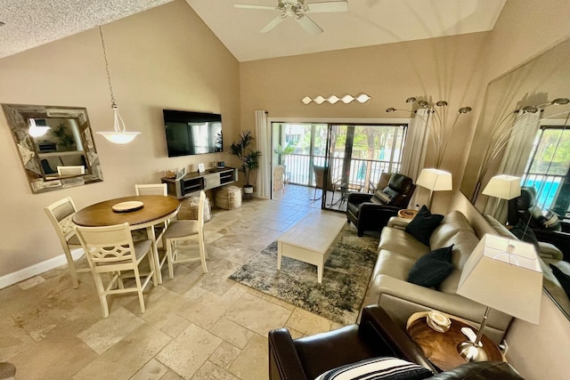 living area featuring plenty of natural light, stone tile floors, baseboards, and high vaulted ceiling