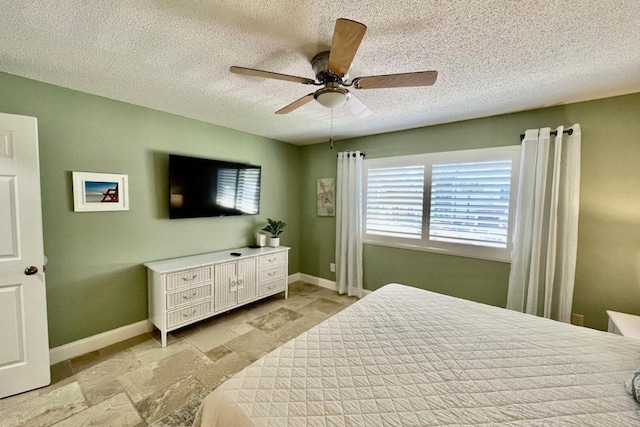 bedroom with stone finish flooring, ceiling fan, a textured ceiling, and baseboards