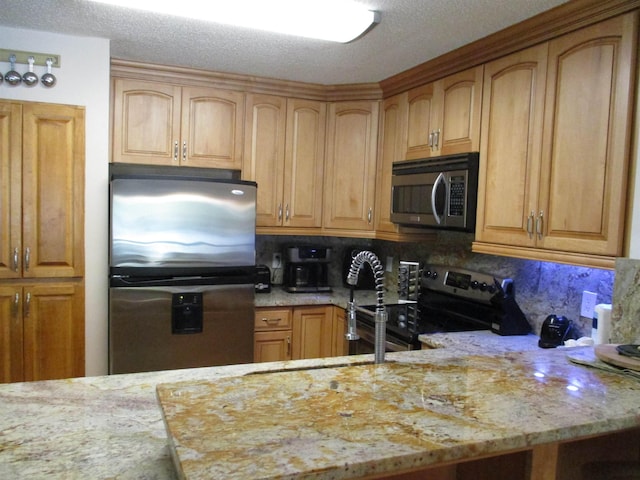 kitchen with a textured ceiling, light stone counters, stainless steel appliances, a sink, and tasteful backsplash