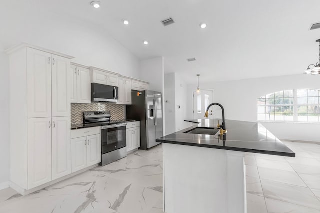 kitchen with dark countertops, a center island with sink, vaulted ceiling, appliances with stainless steel finishes, and a sink