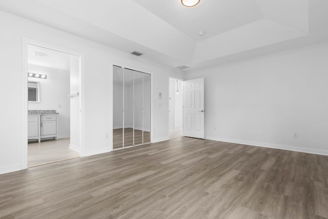 unfurnished bedroom featuring visible vents, a raised ceiling, baseboards, and wood finished floors