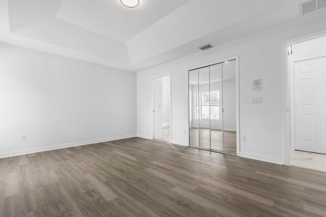 spare room with visible vents, a raised ceiling, baseboards, and wood finished floors