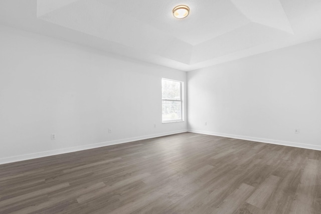 empty room with baseboards, a raised ceiling, and dark wood-style flooring