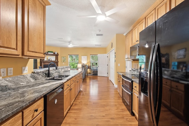 kitchen featuring sink, a textured ceiling, light wood-type flooring, dark stone countertops, and black appliances