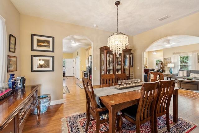 dining space with ceiling fan with notable chandelier and light wood-type flooring