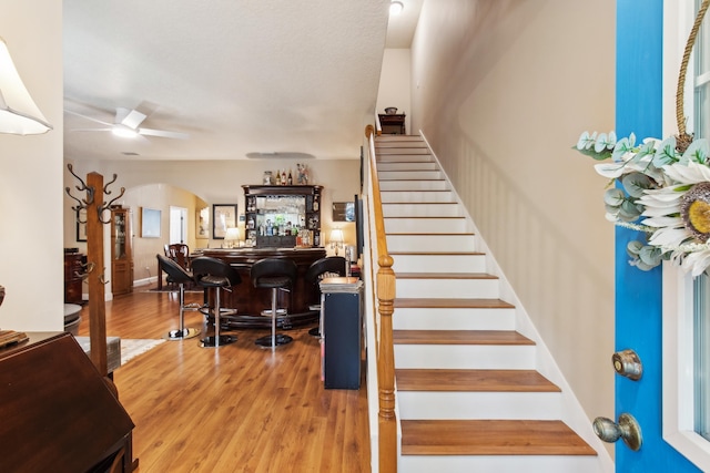 staircase featuring hardwood / wood-style flooring, bar, and ceiling fan