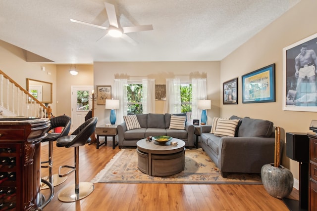 living room with ceiling fan, a textured ceiling, and light hardwood / wood-style flooring