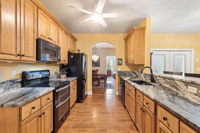 kitchen featuring sink, ceiling fan, dark stone countertops, black appliances, and light hardwood / wood-style floors