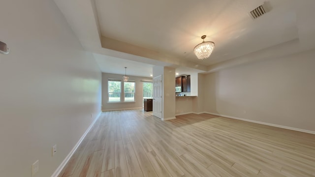 unfurnished living room with light hardwood / wood-style floors, a tray ceiling, and a notable chandelier