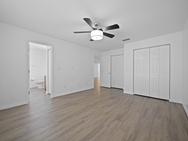 unfurnished bedroom featuring a textured ceiling, ceiling fan, ensuite bathroom, light hardwood / wood-style flooring, and multiple closets