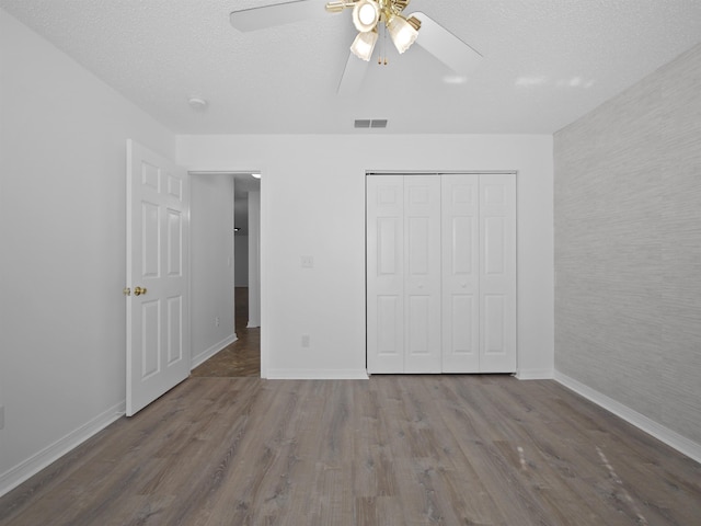 unfurnished bedroom with ceiling fan, a closet, a textured ceiling, and hardwood / wood-style floors