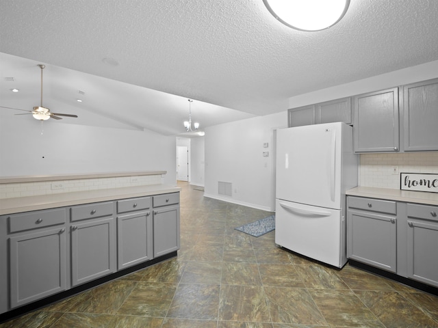 kitchen with lofted ceiling, white fridge, decorative backsplash, gray cabinetry, and ceiling fan with notable chandelier