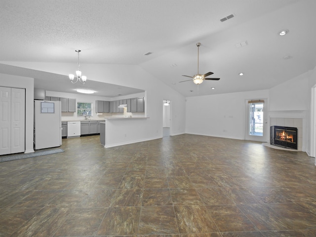 unfurnished living room featuring lofted ceiling, sink, a tiled fireplace, a textured ceiling, and ceiling fan with notable chandelier