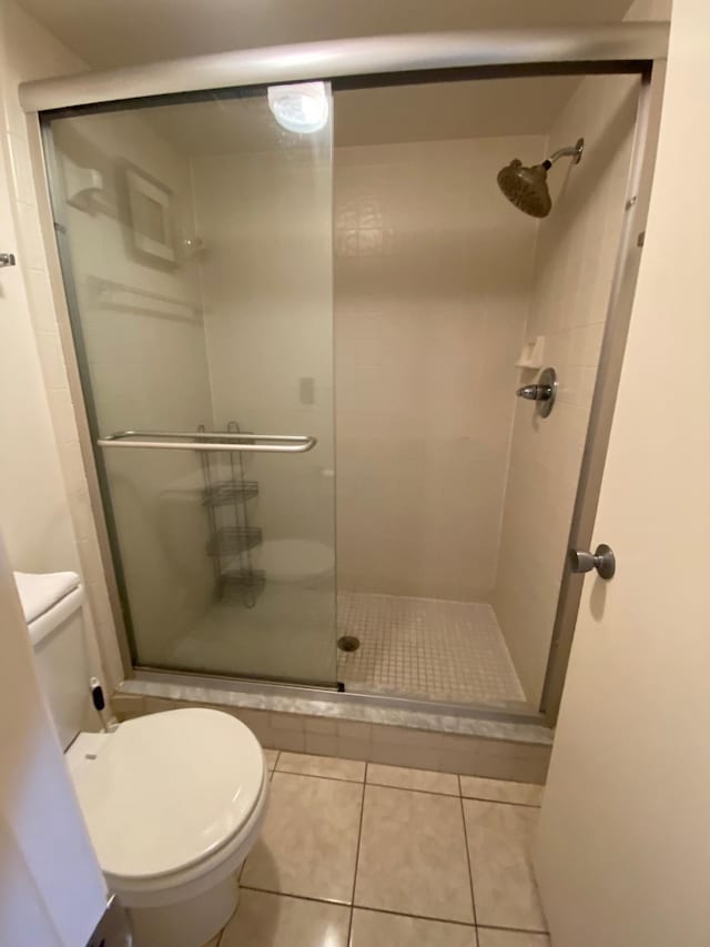 bathroom featuring toilet, tile patterned floors, and a shower with door