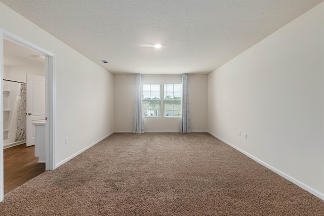 empty room with dark carpet, a textured ceiling, and baseboards