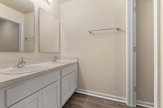 full bath with double vanity, a sink, baseboards, and wood finished floors