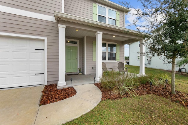 view of exterior entry featuring a garage, a yard, and a porch