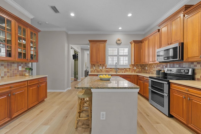 kitchen with crown molding, appliances with stainless steel finishes, a kitchen breakfast bar, a kitchen island, and light hardwood / wood-style floors