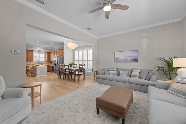 living room with crown molding, ceiling fan with notable chandelier, light hardwood / wood-style flooring, and a textured ceiling