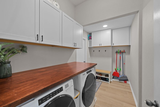 clothes washing area with light hardwood / wood-style floors, washing machine and dryer, and cabinets