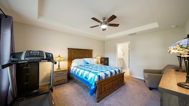 bedroom with carpet floors, a tray ceiling, ensuite bath, and ceiling fan
