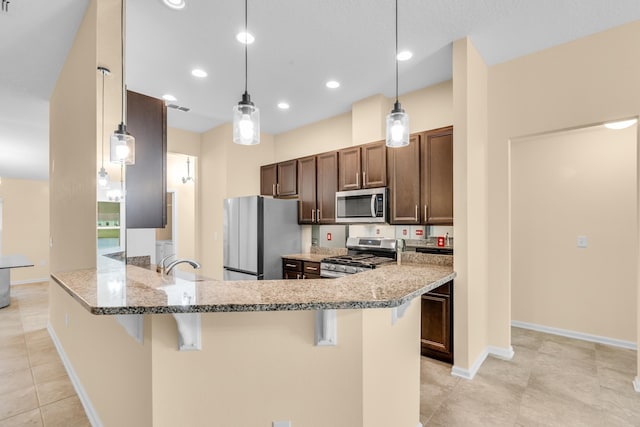 kitchen featuring light stone countertops, pendant lighting, a breakfast bar area, appliances with stainless steel finishes, and light tile patterned flooring