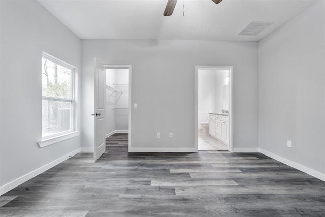 unfurnished bedroom featuring dark wood-type flooring, connected bathroom, a spacious closet, a closet, and ceiling fan