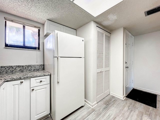 kitchen with white refrigerator, white cabinetry, a textured ceiling, and light hardwood / wood-style flooring