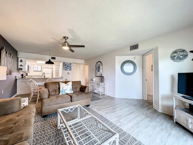 living room with a textured ceiling, light hardwood / wood-style flooring, ceiling fan, and sink