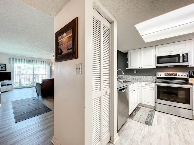 kitchen featuring white cabinets, light wood-type flooring, a textured ceiling, and appliances with stainless steel finishes