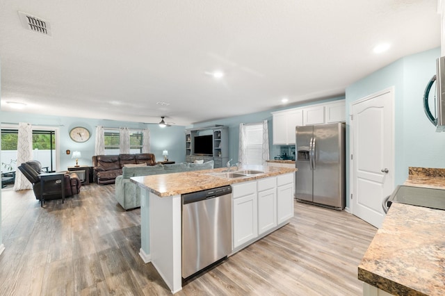 kitchen with appliances with stainless steel finishes, ceiling fan, sink, white cabinets, and an island with sink