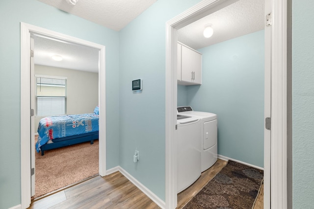 laundry room featuring washer and clothes dryer, cabinets, a textured ceiling, and light hardwood / wood-style flooring