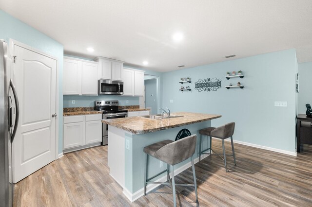 kitchen featuring a center island with sink, white cabinets, sink, appliances with stainless steel finishes, and a breakfast bar area