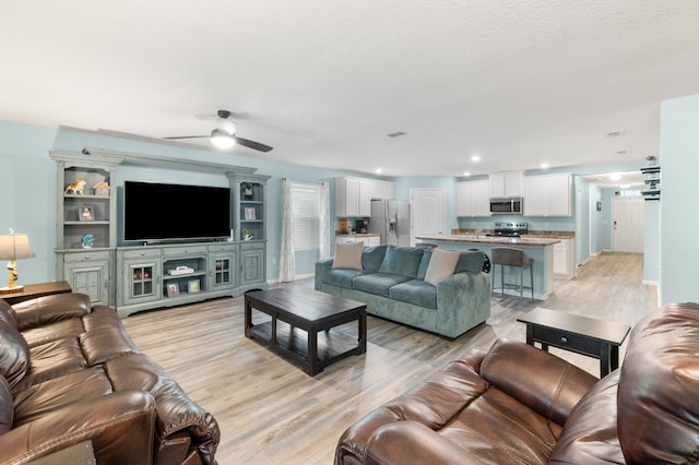 living room with ceiling fan, light hardwood / wood-style floors, and a textured ceiling