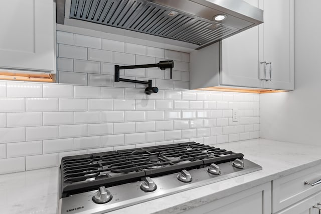 kitchen with light stone counters, wall chimney exhaust hood, stainless steel gas cooktop, and white cabinets