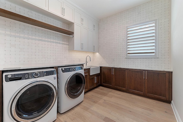 clothes washing area featuring cabinets, independent washer and dryer, sink, and light hardwood / wood-style floors