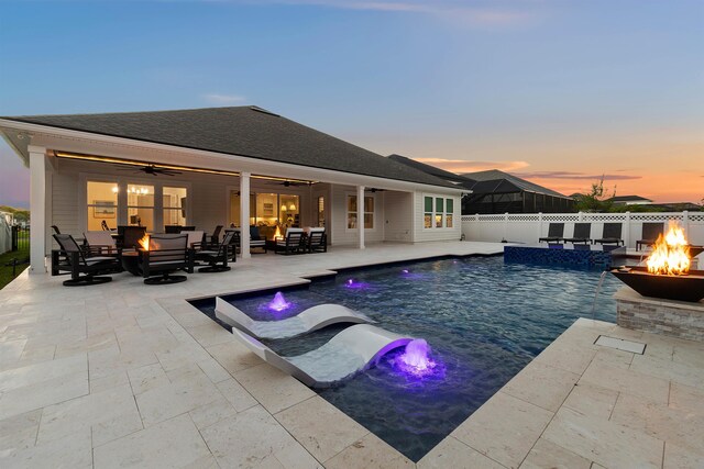 pool at dusk with a patio, pool water feature, an outdoor living space with a fire pit, and ceiling fan