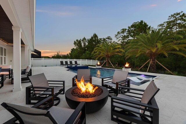 pool at dusk with a patio, pool water feature, and a fire pit