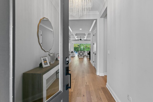 hallway with beam ceiling, coffered ceiling, a chandelier, and light wood-type flooring