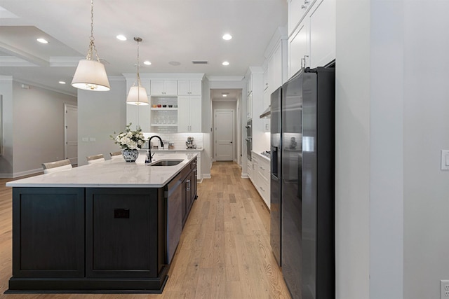 kitchen with sink, stainless steel fridge, white cabinets, a center island with sink, and decorative light fixtures