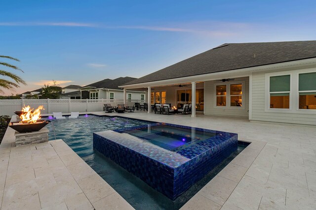 pool at dusk featuring an in ground hot tub, ceiling fan, a patio, and a fire pit