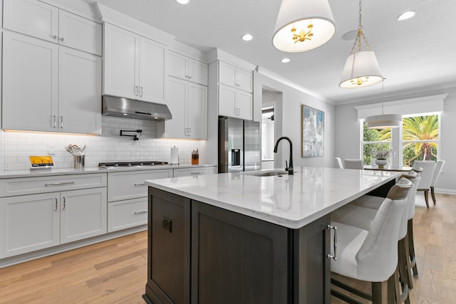 kitchen with pendant lighting, sink, appliances with stainless steel finishes, white cabinetry, and a center island with sink