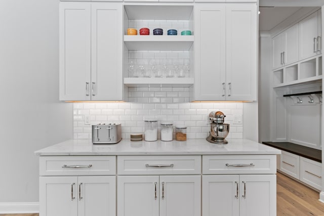 kitchen with white cabinetry, light stone countertops, light hardwood / wood-style floors, and tasteful backsplash