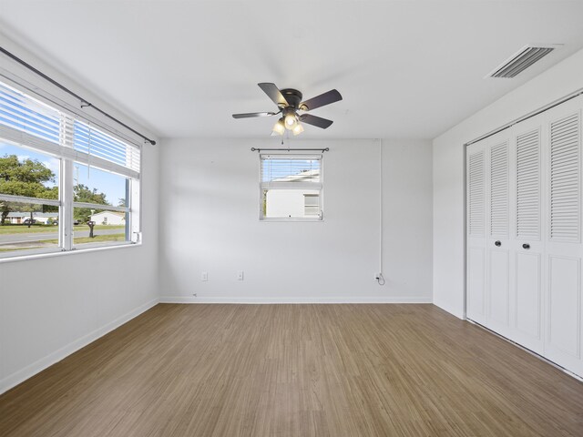 unfurnished bedroom with multiple windows, a closet, hardwood / wood-style flooring, and ceiling fan