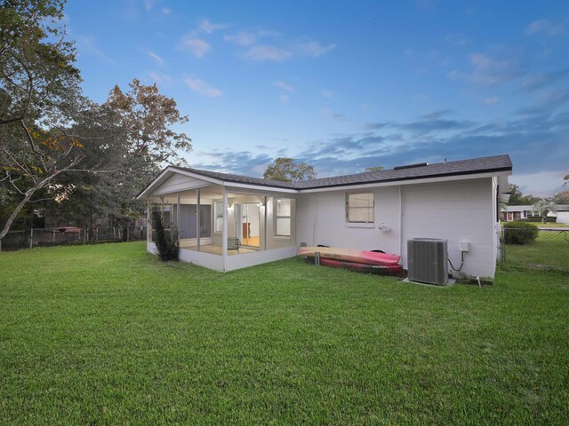 rear view of house with central air condition unit, a lawn, and a sunroom