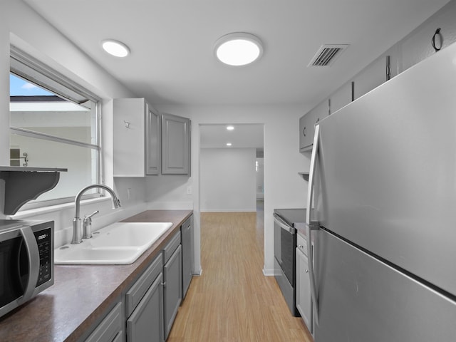 kitchen with gray cabinets, sink, light hardwood / wood-style flooring, and appliances with stainless steel finishes