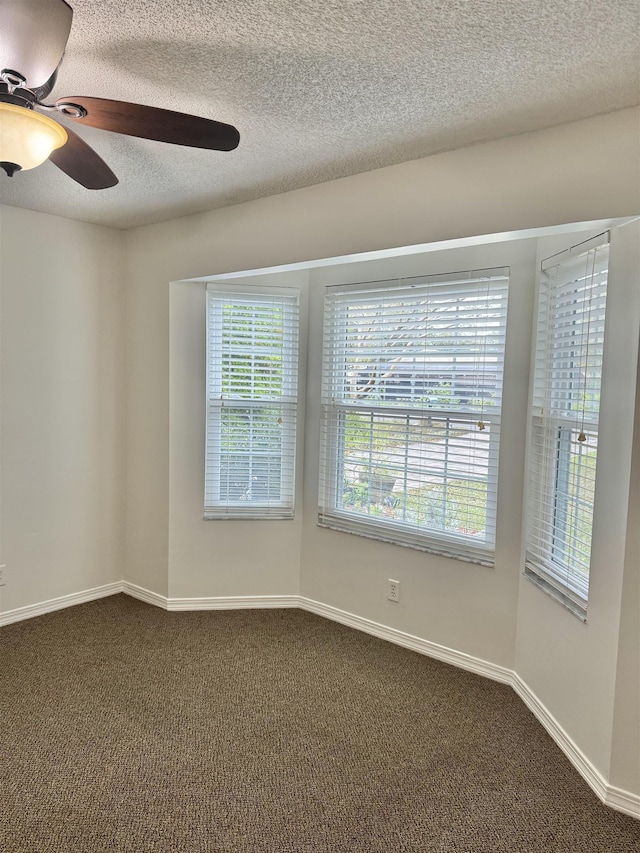 empty room featuring a ceiling fan, baseboards, dark carpet, and a textured ceiling