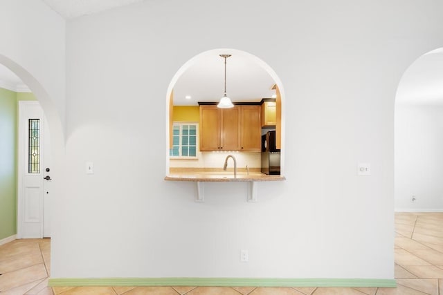 kitchen with baseboards, a breakfast bar, light tile patterned floors, refrigerator, and a sink